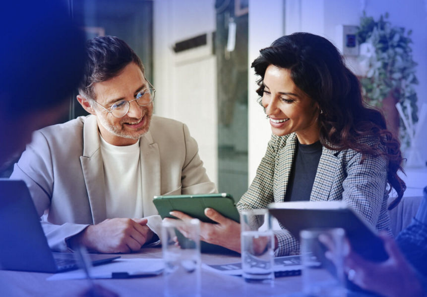 Professionals sitting in a meeting, exploring modernised apps on a digital tablet.