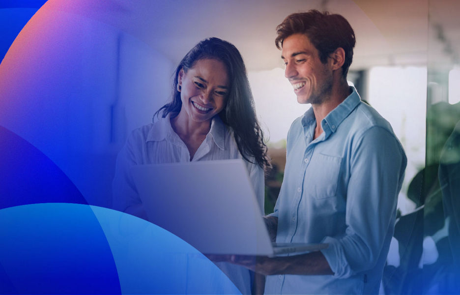 Two colleagues smiling while looking at a laptop, collaborating on digital projects.
