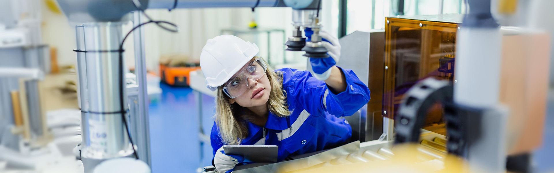 Woman working in manufacturing plant, wearing blue suit and safety helmet and glasses and holding tablet