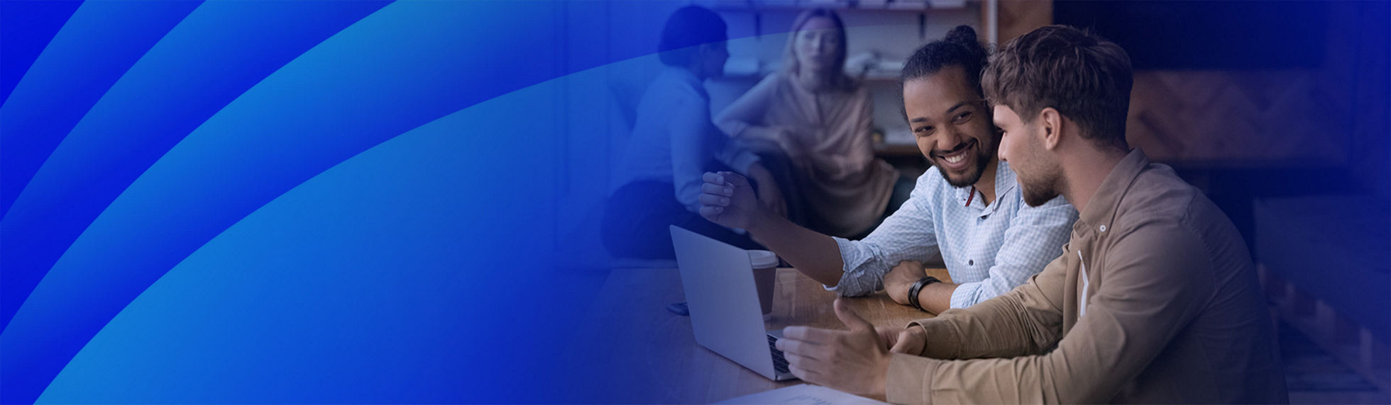 A blue layered gradient lens pattern overlaying an image of two young men sitting at a wooden table in a modern office space, engaged in a lively discussion while looking at a laptop. 