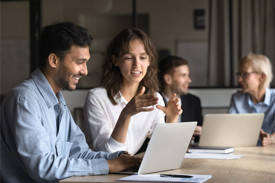 Two work colleagues having a conversation at a table while looking at a laptop