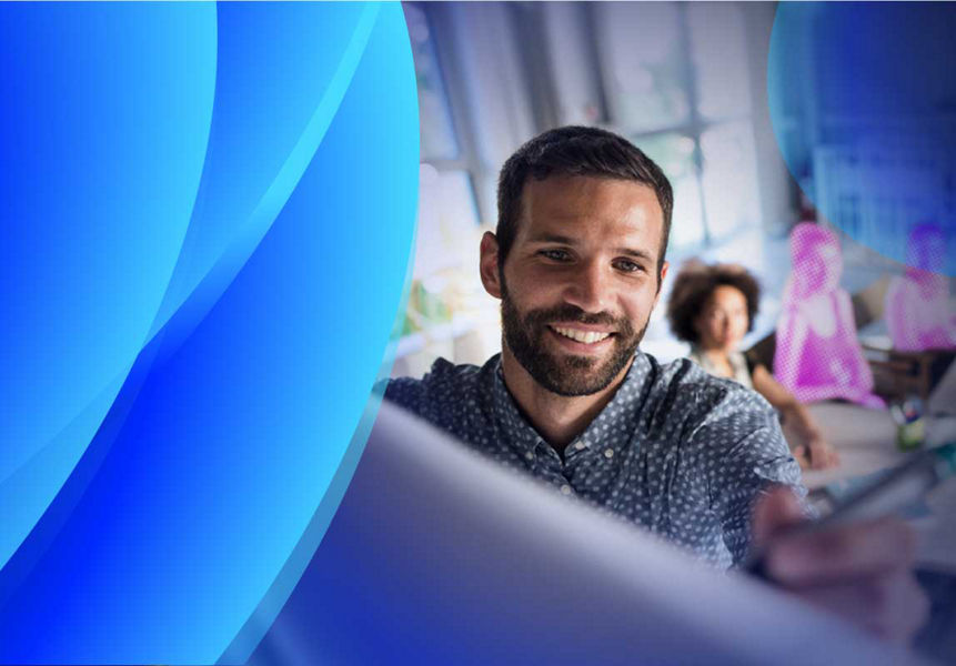 A smiling man writing on a board with women in the background