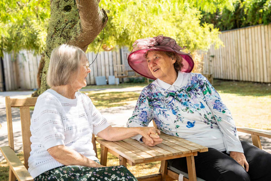 Two women interacting on an Alden Care Home bench