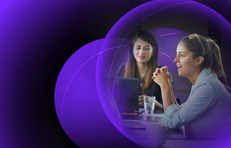 A woman smiling while sitting at a desk in meeting room with her colleagues