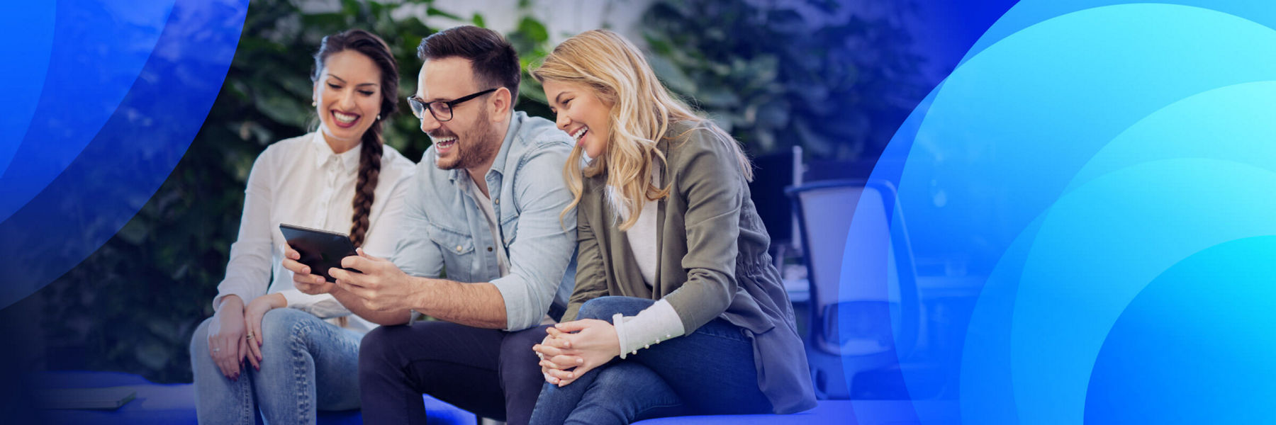 Three people sitting together smiling while looking at a device.