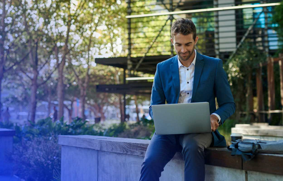 A man sitting on a concrete bench looking at a laptop.