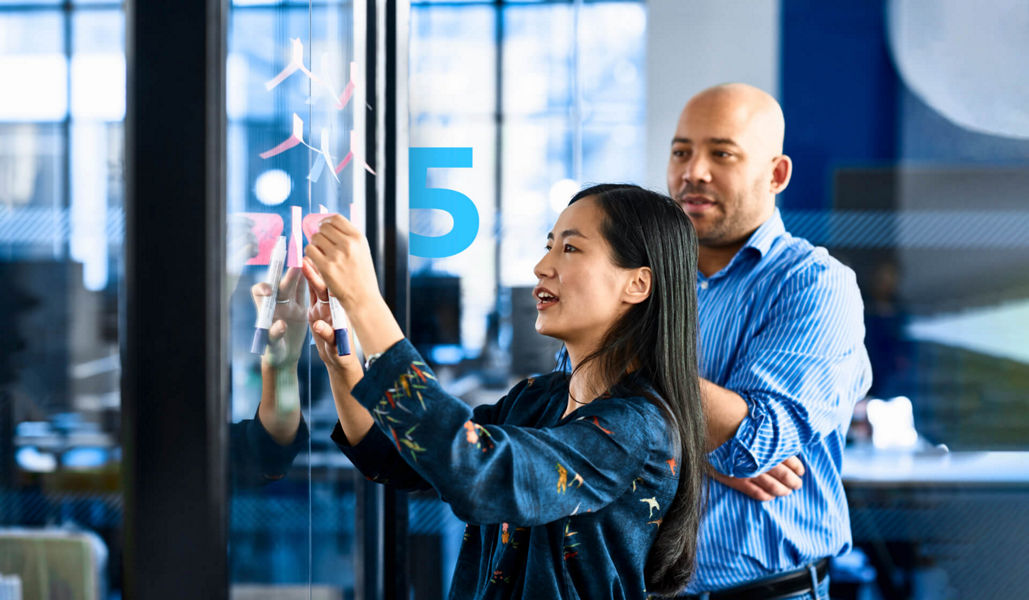 Two professionals in an AI brainstorming session, using sticky notes on a glass wall