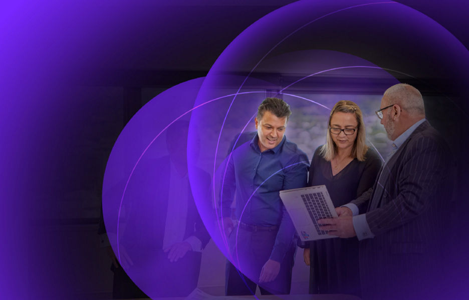 Three individuals looking and talking at a touch screen laptop while standing