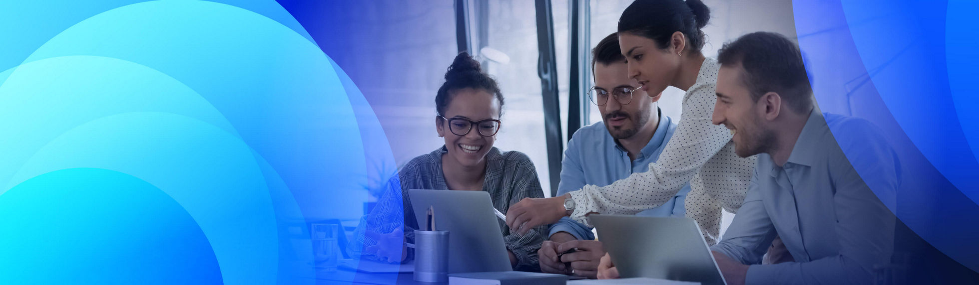a team in the office around a laptop with a woman pointing at something on the screen
