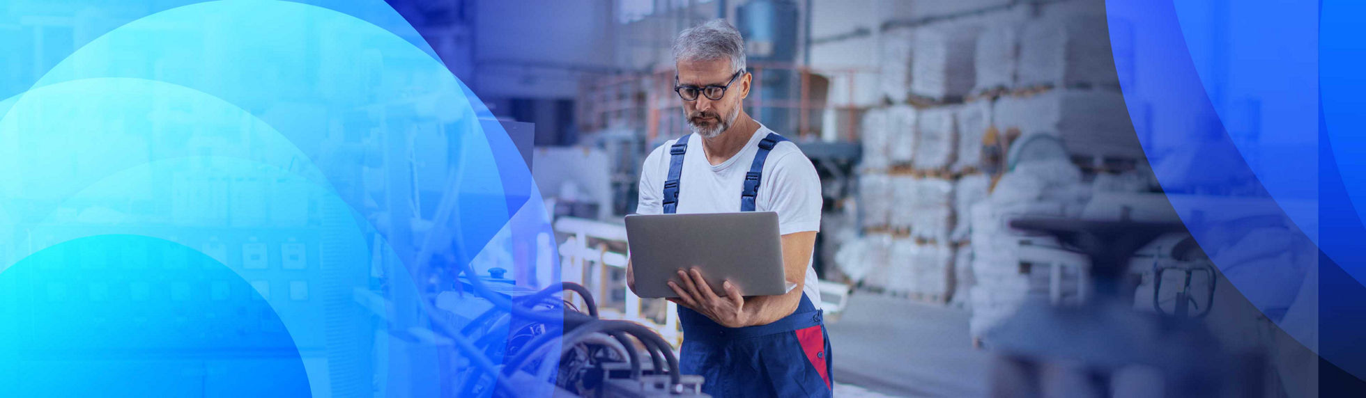 A technician in a warehouse monitoring processes on a laptop