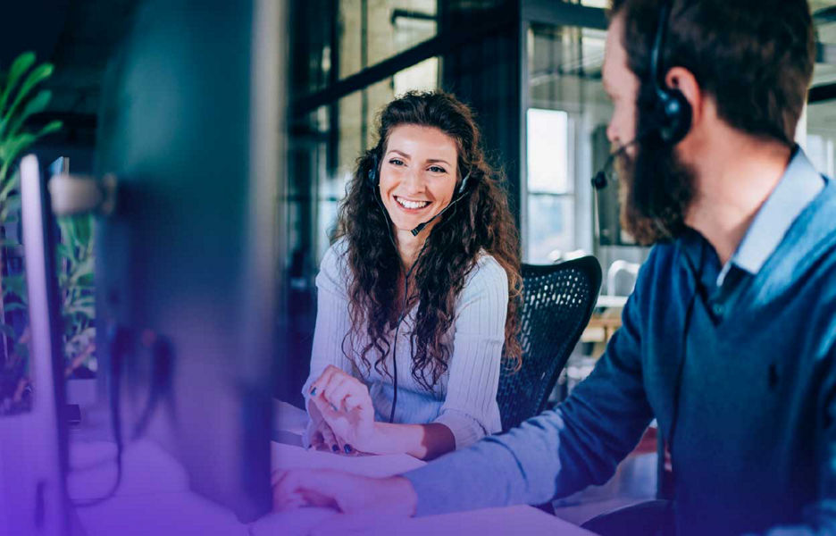 Women and man with headsets on looking a monitor screen and smiling 