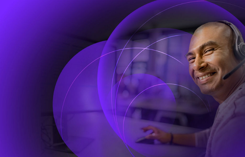 A man smiling while wearing a headset at his desk in an office