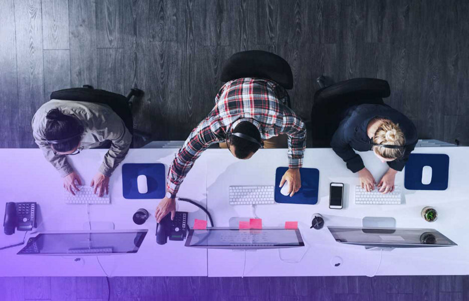 Aerial view office desk with 3 workers working on monitors