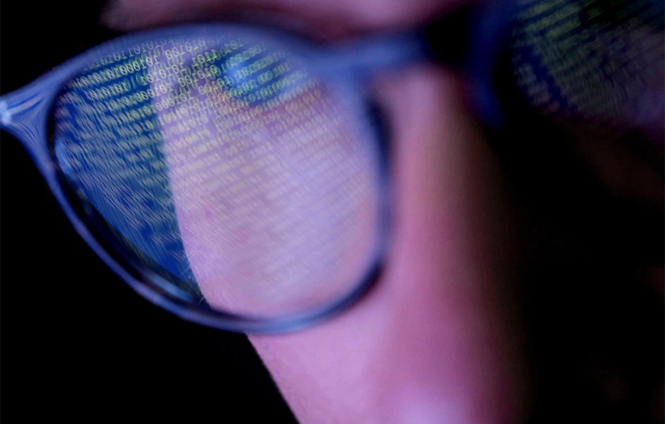 A close up shot of a person wearing glasses with code reflecting in the lenses