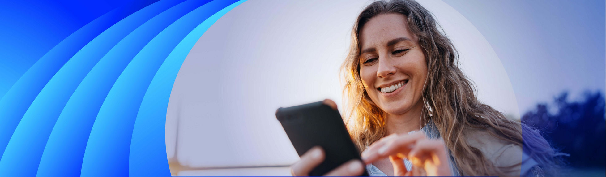 Woman walking outside, holding a mobile phone and smiling warmly.