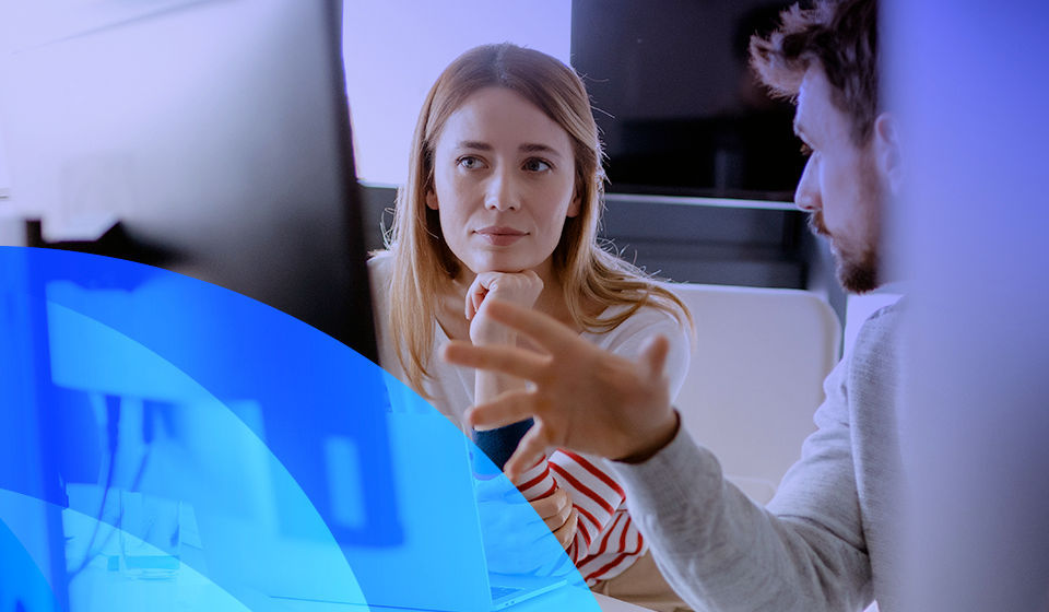 lady looking and computer screen with a man sitting beside her, talking using hand gestures