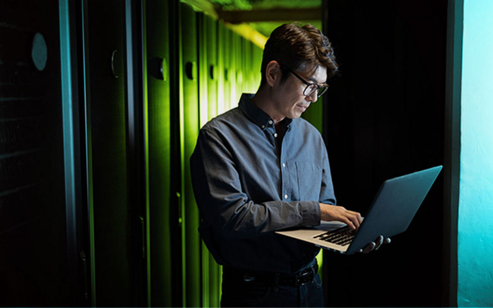 Software expert working on a laptop in a server room