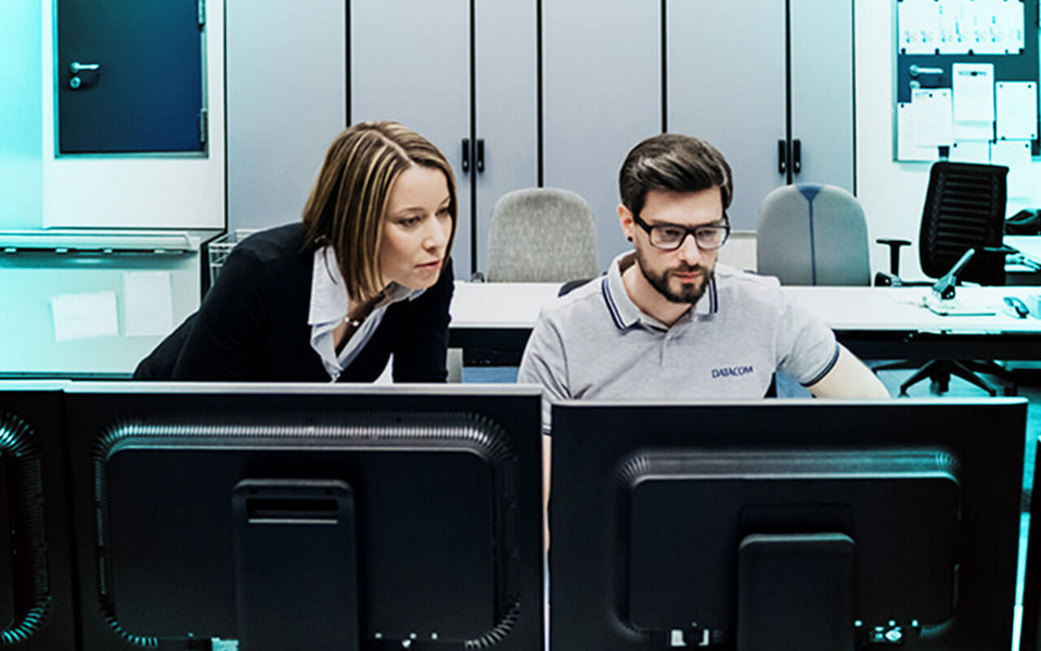 Two tech professionals working in front of multiple computers