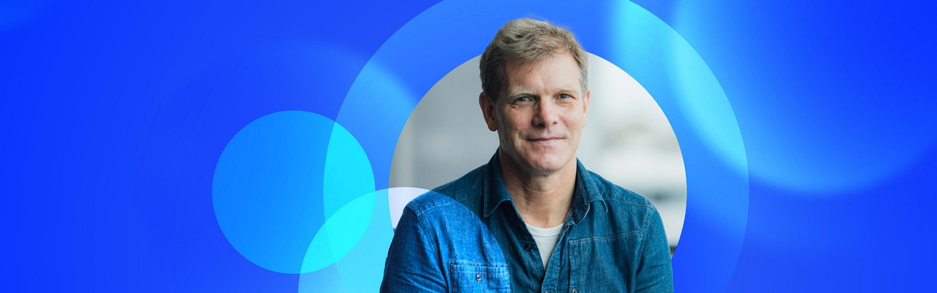 Greg Davidson sitting down with a blue lens graphic floating behind him