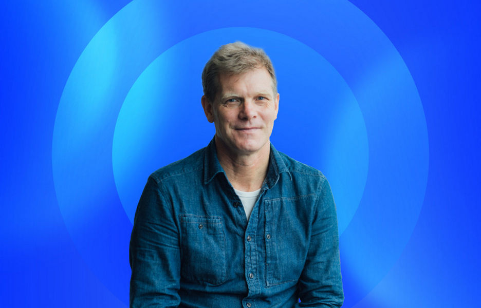 Greg Davidson sitting down with a blue lens graphic floating behind him