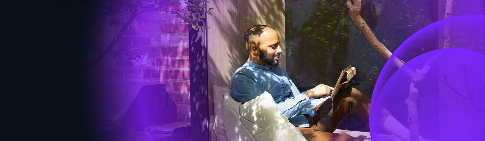 Smiling man reading on tablet at cosy window seat