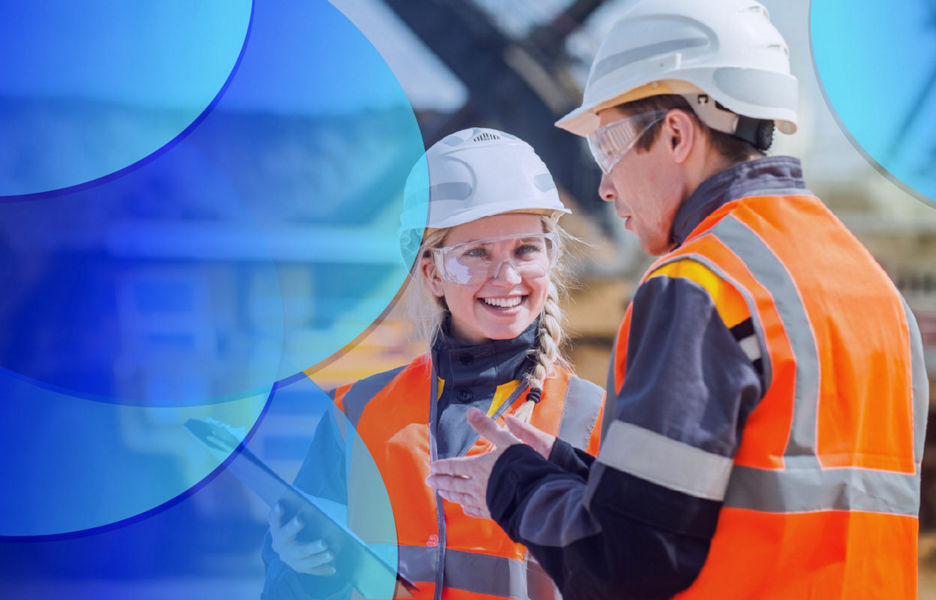 Two colleagues talking to each other while wearing protective gear at a site while looking at plans