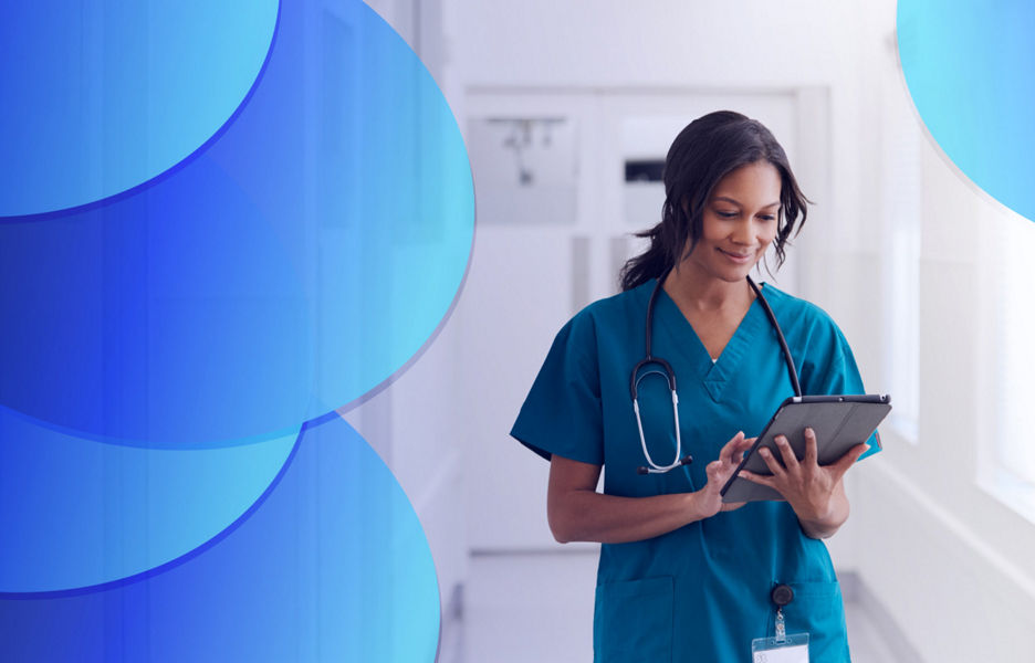 Woman in a hallway at a hospital wearing scrubs and using an iPad