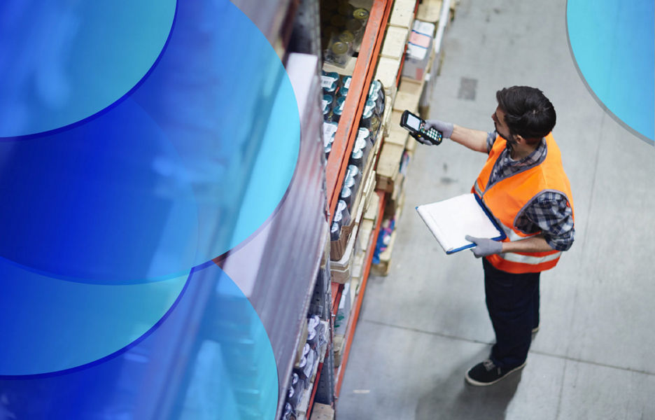 A man in a warehouse holding a scanner and clipboard while looking at products