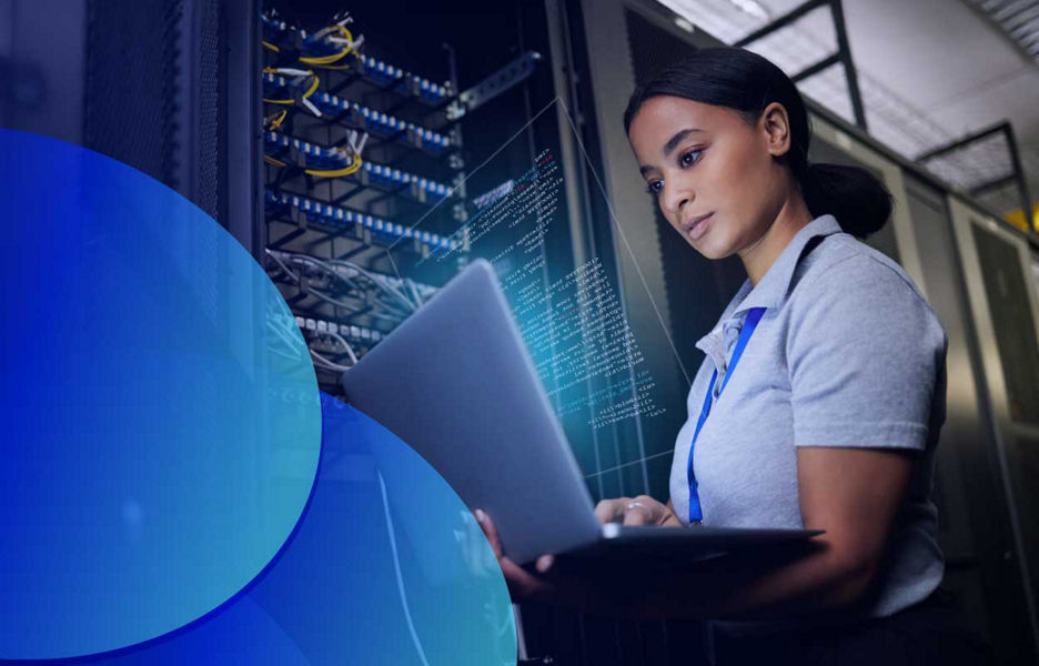 A woman standing, working on laptop screen in a data centre