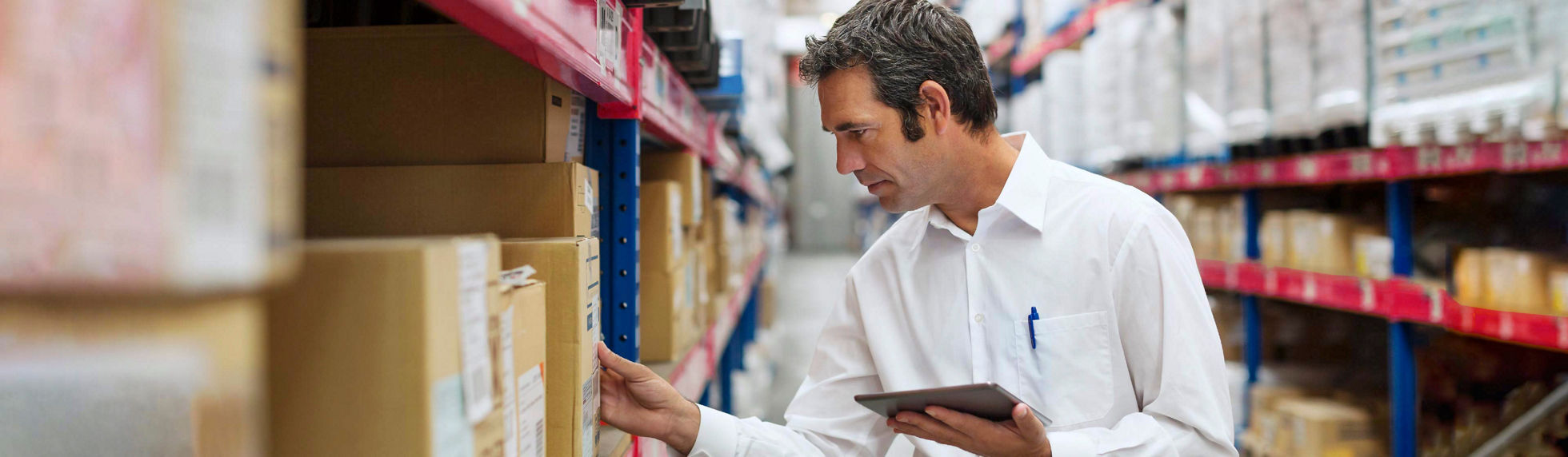 A man in a warehouse taking stock of boxes on a tablet