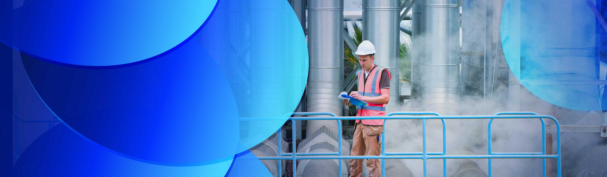 A worker standing on a walkway in front of large power station pipes