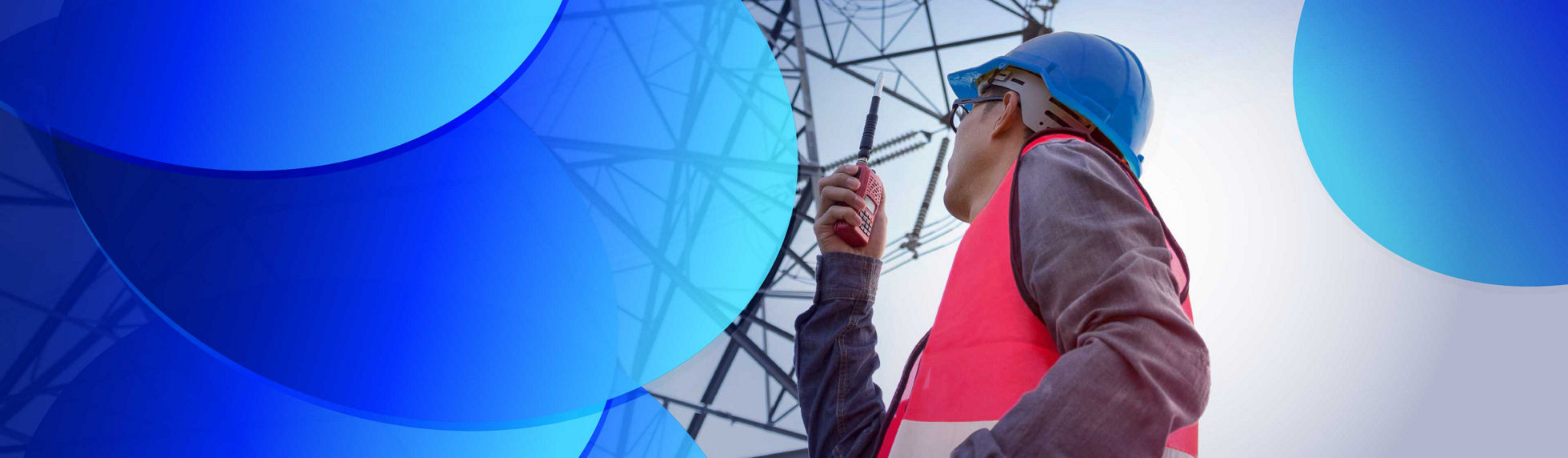 A worker standing below a transmission tower holding a walkie talkie