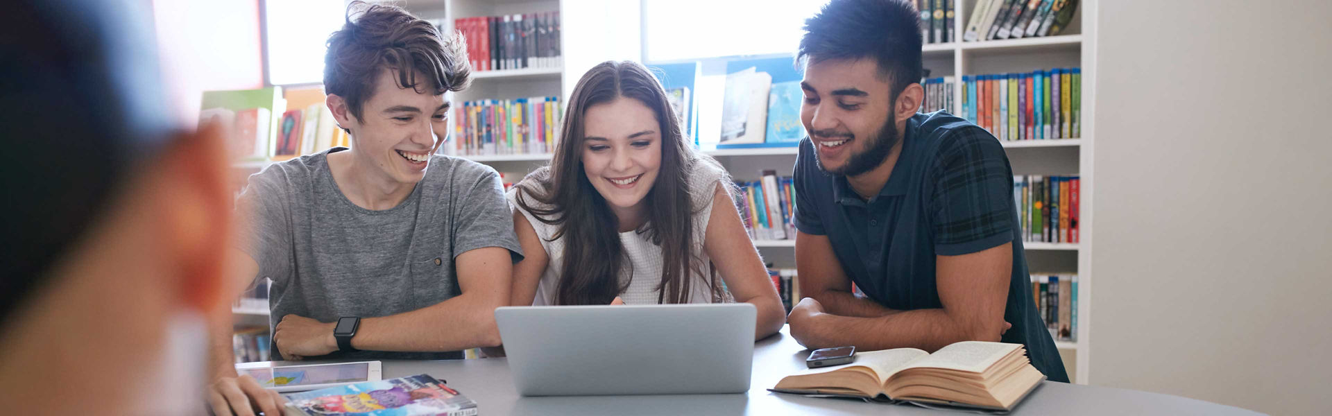 Three teenagers using a laptop in a library