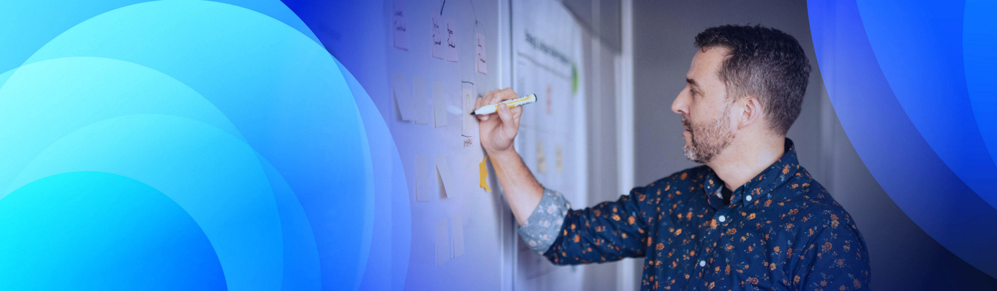 A man writing on a sticky note stuck to a board