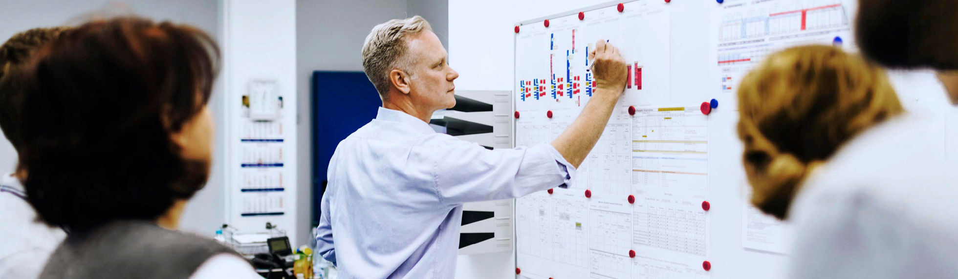 A man writing on a whiteboard in a team meeting