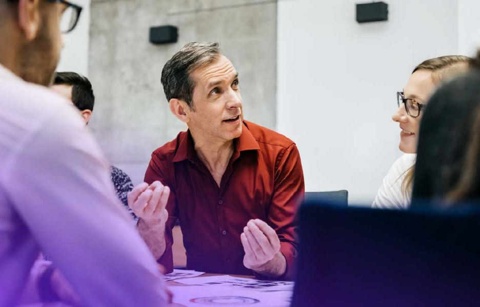 Man in a meeting room talking while people around him listen