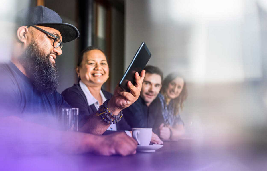 Group of people sitting in a table drinking coffee while one is looking at a tablet screen