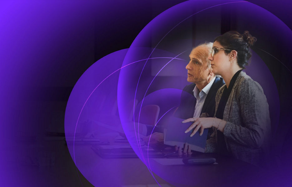 Two work colleagues sitting on one side of a table in a board room talking to two others across the table