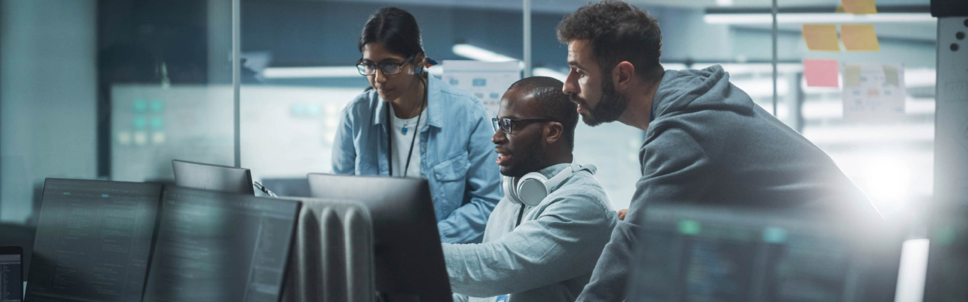A diverse team of three professionals collaborating at computers in a modern office environment