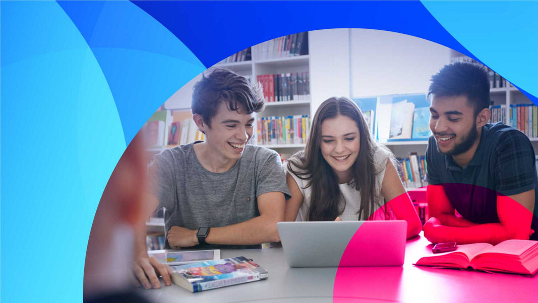 Three smiling graduates looking at a laptop