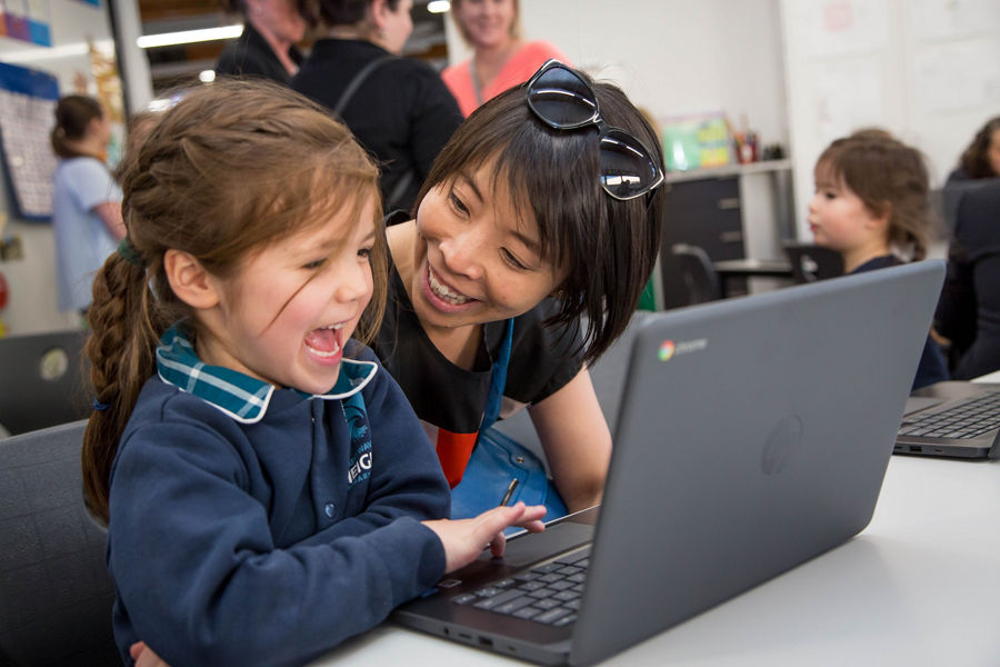 A teacher holding a laptop with children around