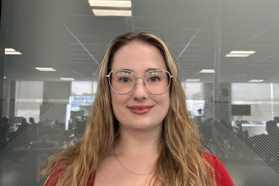 Headshot of Becky Dent standing in an office setting smiling, wearing glasses and a red top