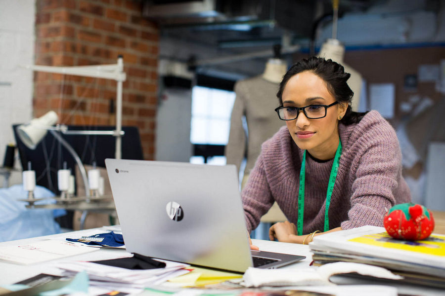 A young woman working on her laptop in a clothing studio