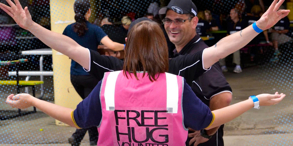 A man and a woman wearing a pink vest that says "Free hugs" 