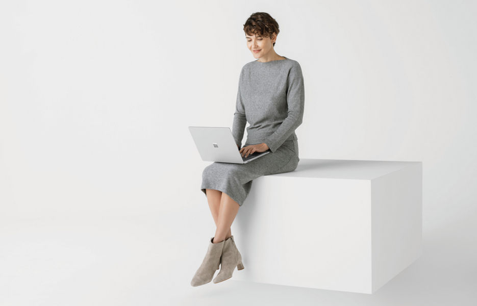 Woman sitting on white box, typing on a Windows laptop