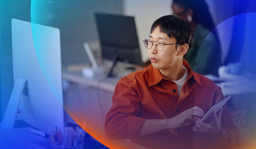 Young man in the office with a tablet in hand and looking at his desktop computer screen