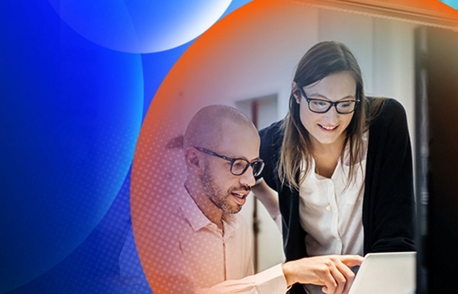 A woman standing and a man sitting at his desk looking and pointing at a laptop screen in an office with an orange and blue lens overlay