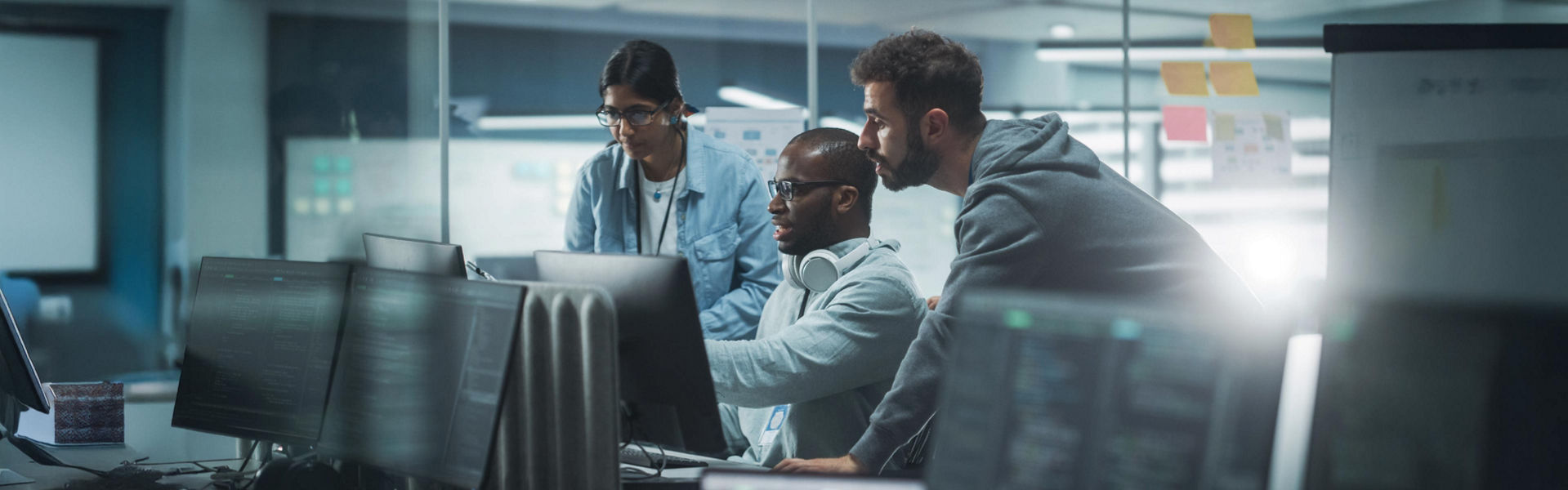 Three coworkers talking and pointing at a computer in an office.