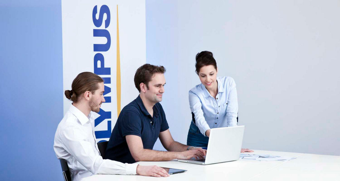 Three Olympus employees working in front of an Olympus banner