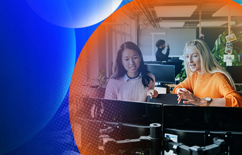 Two woman standing while having a conversation and looking at two monitors in an office with an orange and blue lens overlay